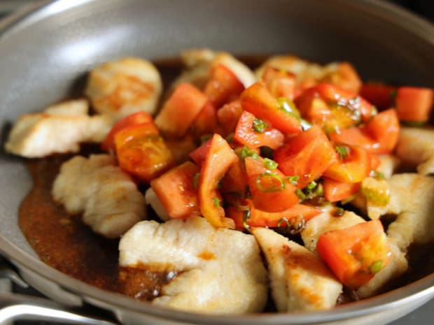 フライパンで焼いた鶏むね肉の上に、トマトとねぎの甘辛だれをかけている様子 フライパンで焼いた鶏むね肉の上に、トマトとねぎの甘辛だれをかけている様子