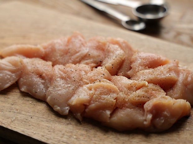 塩とこしょうで下味をつけた鶏むね肉のそぎ切りが木製のまな板に並べられている様子 塩とこしょうで下味をつけた鶏むね肉のそぎ切りが木製のまな板に並べられている様子