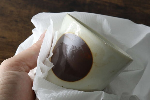 キッチンペーパーで茶色の模様がある器を拭いている手