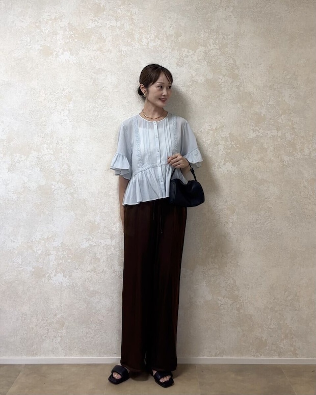 ブルーのフリルシャツと黒バッグを着用した女性の全身