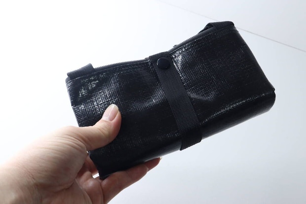 女性の手が、コンパクトに折りたたまれた黒いトートバッグを持つ