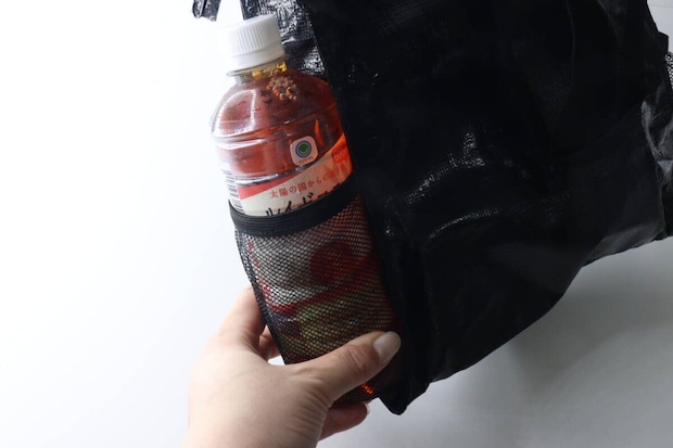 黒いトートバッグのサイドメッシュポケットにペットボトル飲料を入れる