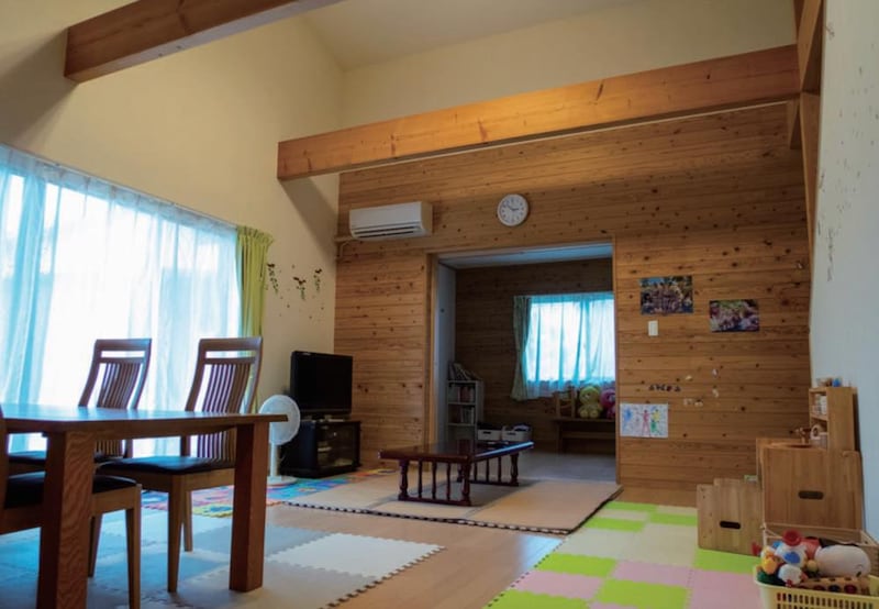 「子どもショートステイ」専用の家の内観。木を基調としたリビングダイニングルーム。木製のダイニングテーブルと椅子、テレビなどが置かれている