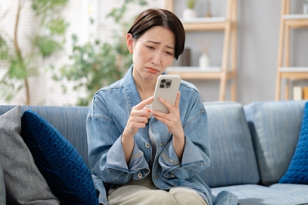 女性　困り顔　スマホ　ソファ